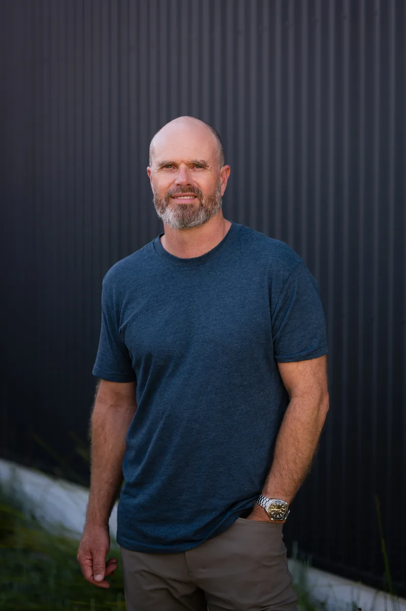 Ben Caine, Perth-based architect and founder of Speki, standing in front of a dark corrugated wall.